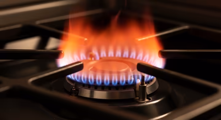 A close-up macro shot of a hot surface igniter for a gas oven, glowing bright orange-red.