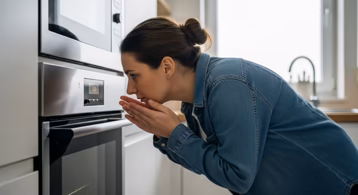A person with a concerned expression cautiously sniffing the air near their kitchen oven.
