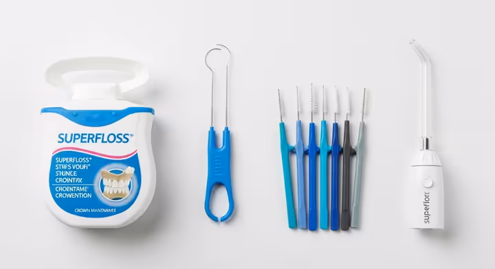 An array of home-care tools for cleaning around dental crowns, including Superfloss, interdental brushes, and a water flosser.